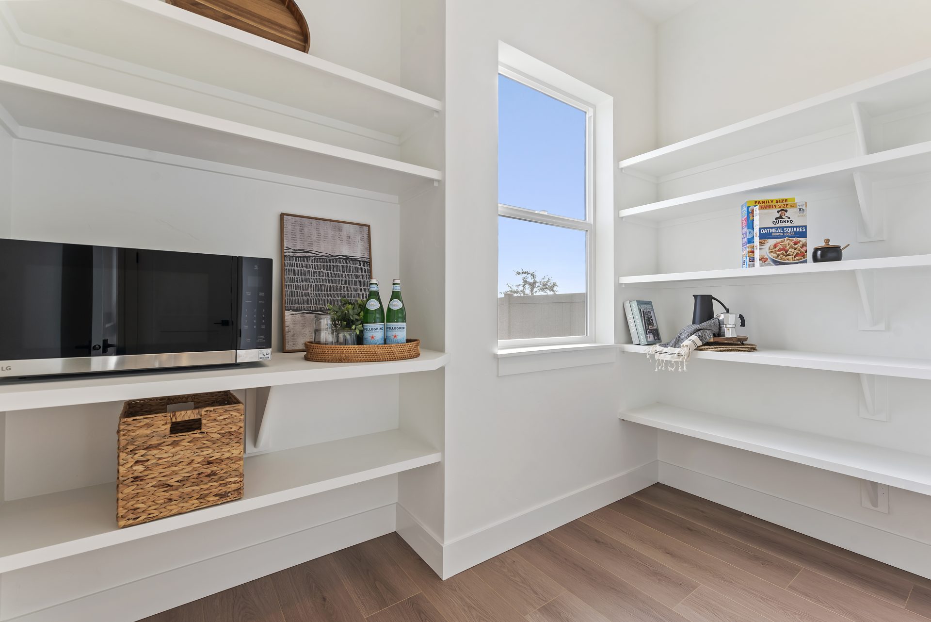 A large walk in pantry with multiple shelves, a microwave on one of the shelves and a window.