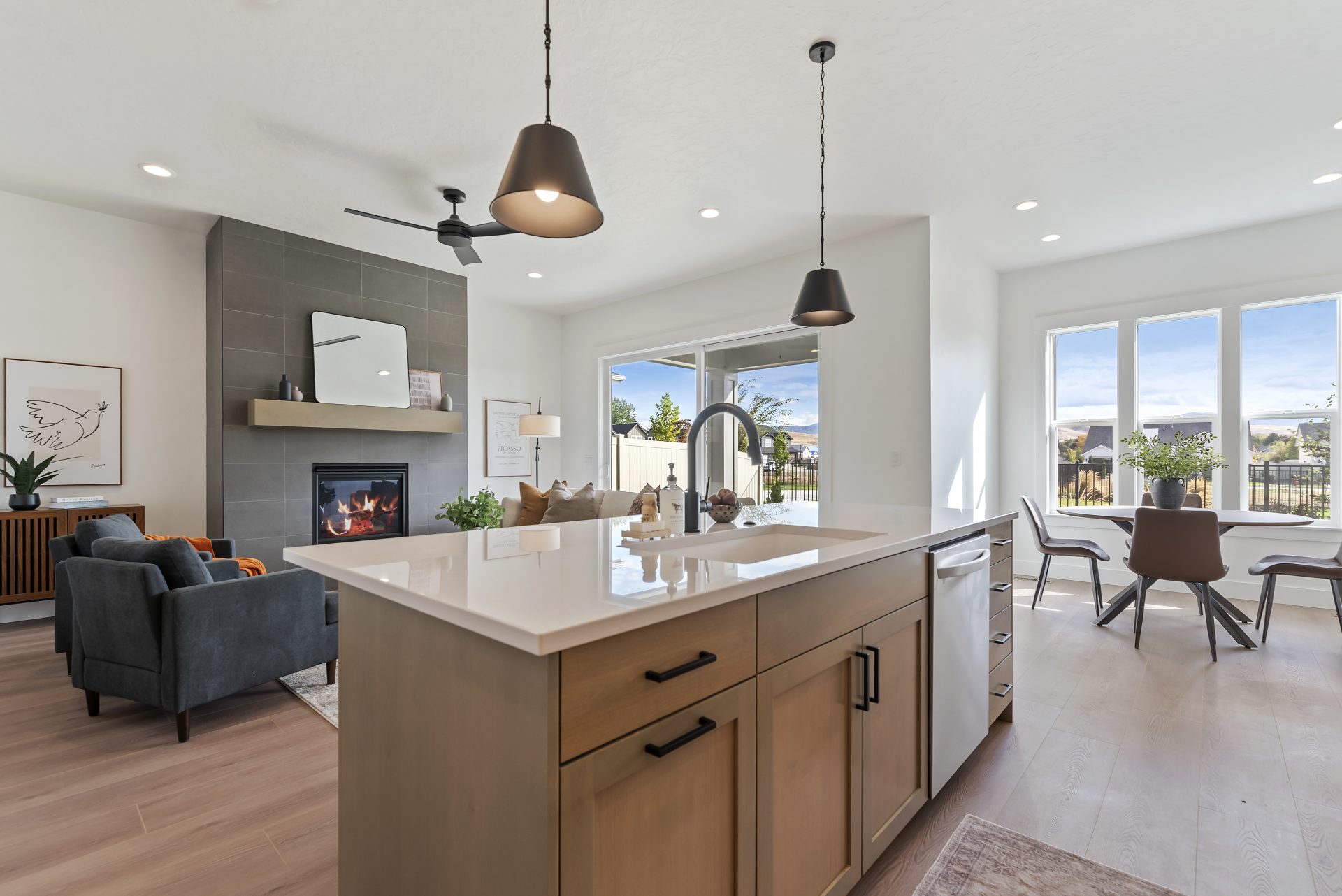 View of a kitchen island straight ahead with a brown stained wood base, light color countertop, with a sing and faucet. Behind the island is a family room with blue color chairs and a fireplace with floor to ceiling tile detail and a mantle and a sliding 