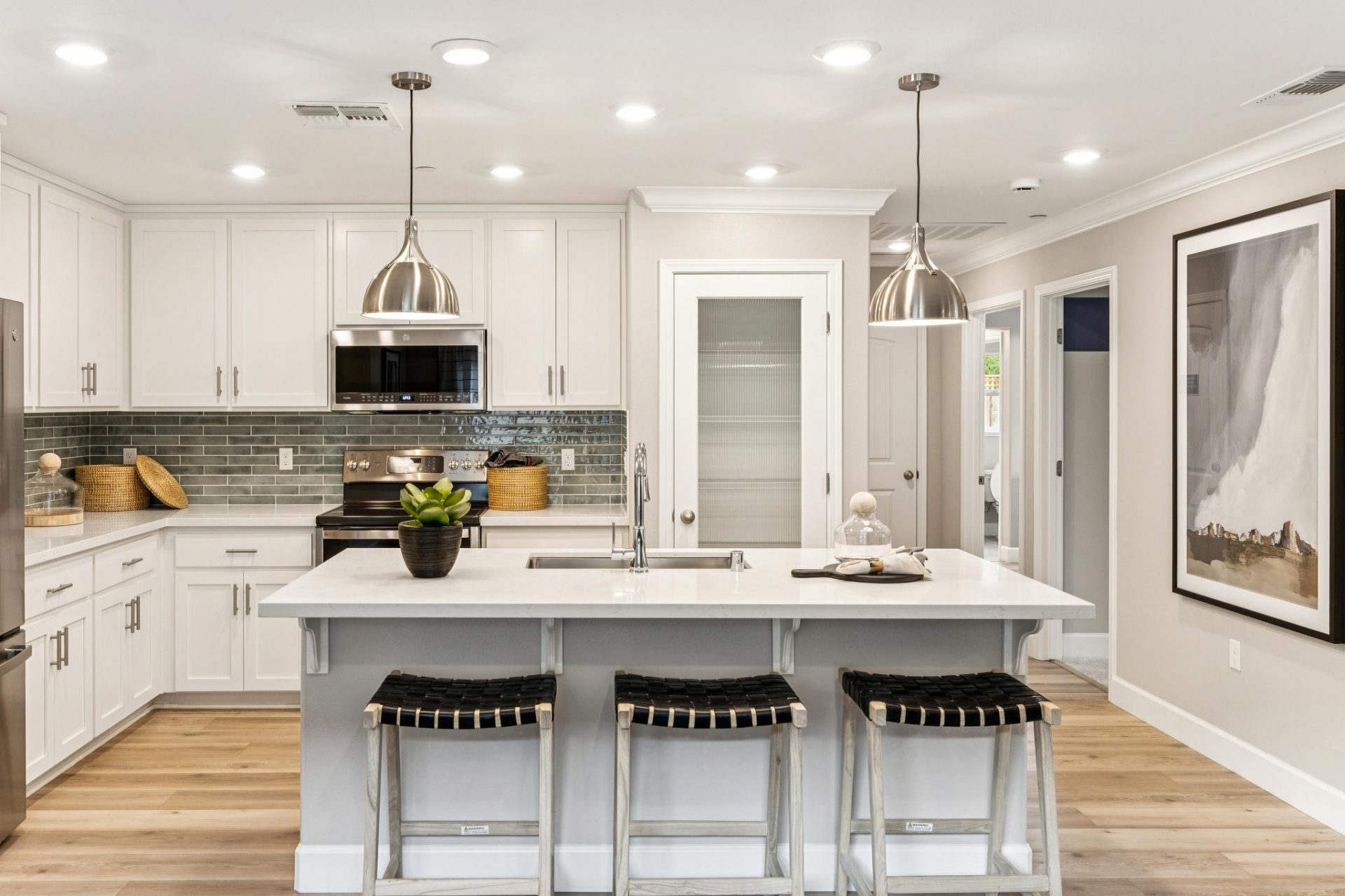 Open kitchen with hight beech wood cabinetry, tiled backsplash, white quartz countertops, kitchen island with 3 counter stools, hardwood floors, 9 foot ceilings with canned lights, 8 foot pantry door, and designer pendants over the island.