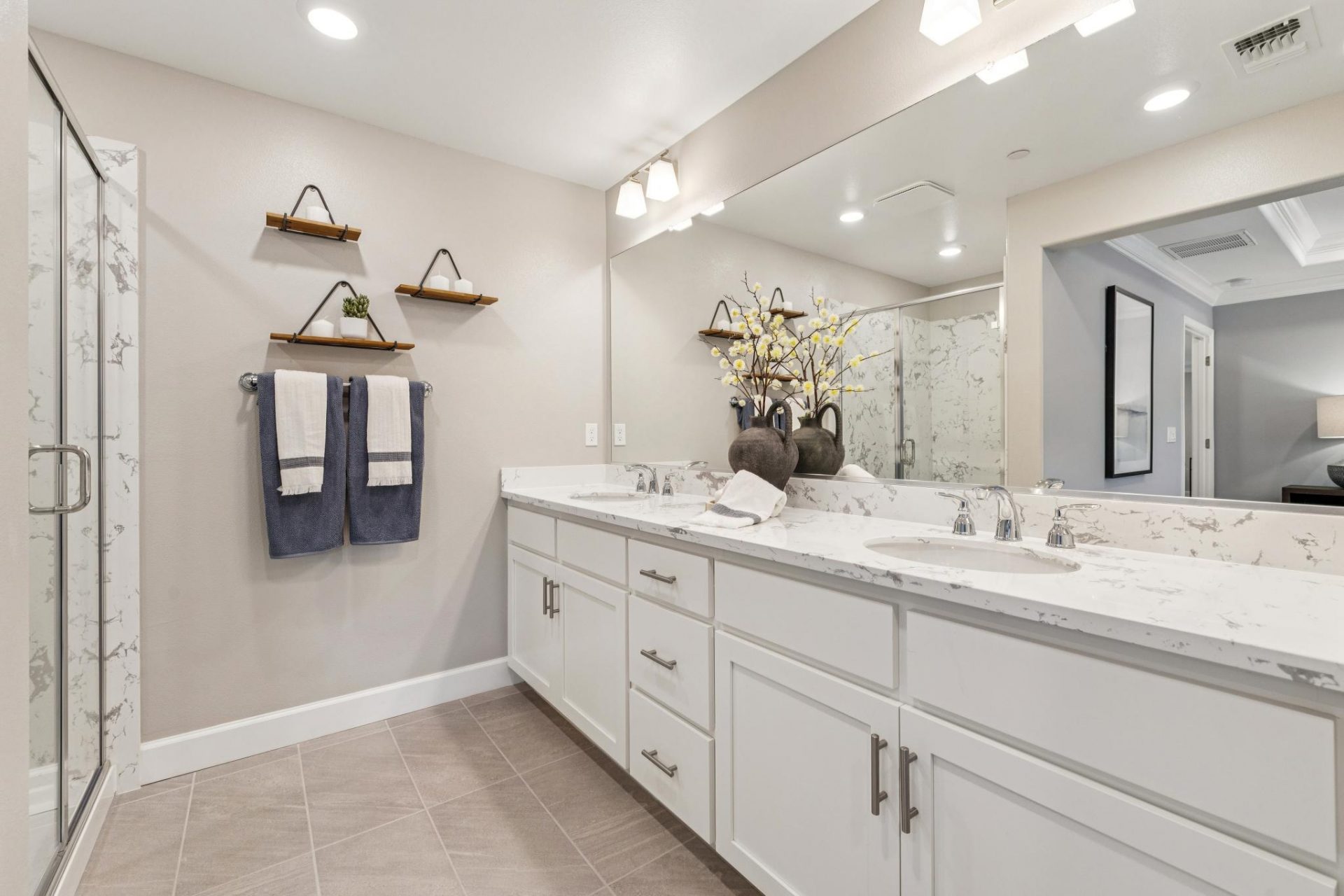 Primary bathroom with tiled flooring, dual sink vanity and sconces over the mirror, white beech wood cabinetry, white quartz countertops, tiled walk-in shower with glass doors, and 9 foot ceiling with canned lights.