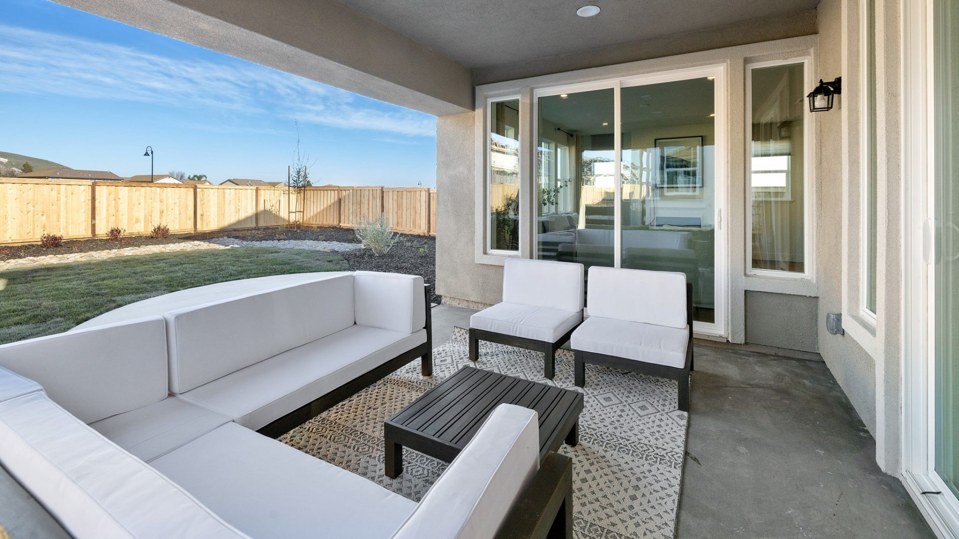A view of the back porch with an area rug and outdoor furniture; a sectional shaped couch, two chairs and a table. A glass sliding door is accessible from this area.