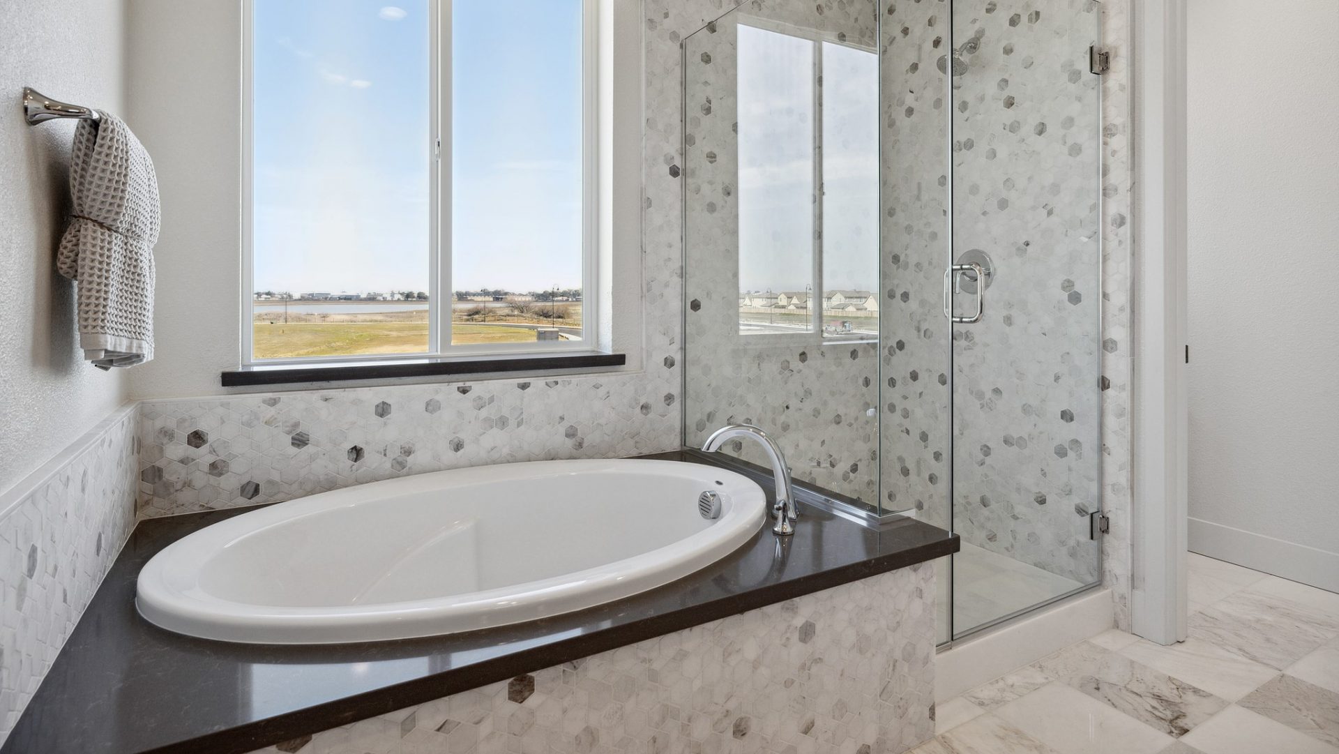 A bathroom tub and shower stall with glass, including stone detailing from floor to ceiling and wrapped around a sit in tub with chrome fixtures and a large window located above the tub.