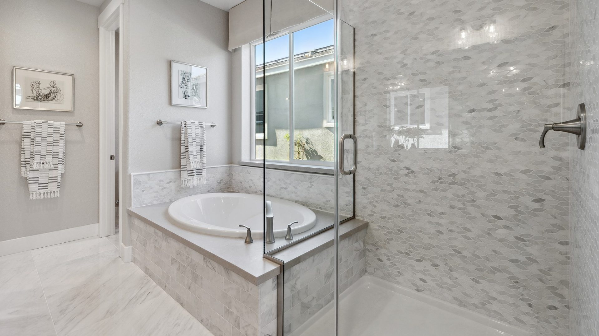 A spa like bathroom with a large soaking tub with a large window located above it. To the right, a shower enclosure with multi colored tiles leading to the ceiling and light colored tile flooring.