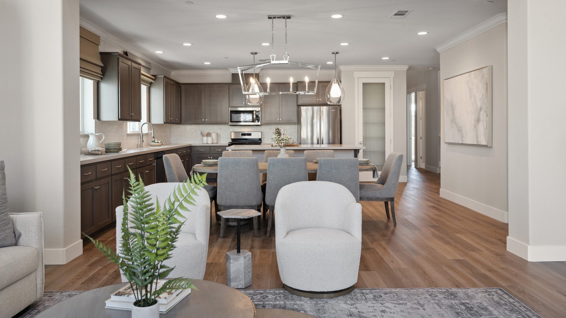Far view of dining room and kitchen with lots of cabinetry, a large chrome finish chandelier and two hanging pendant light fixtures.