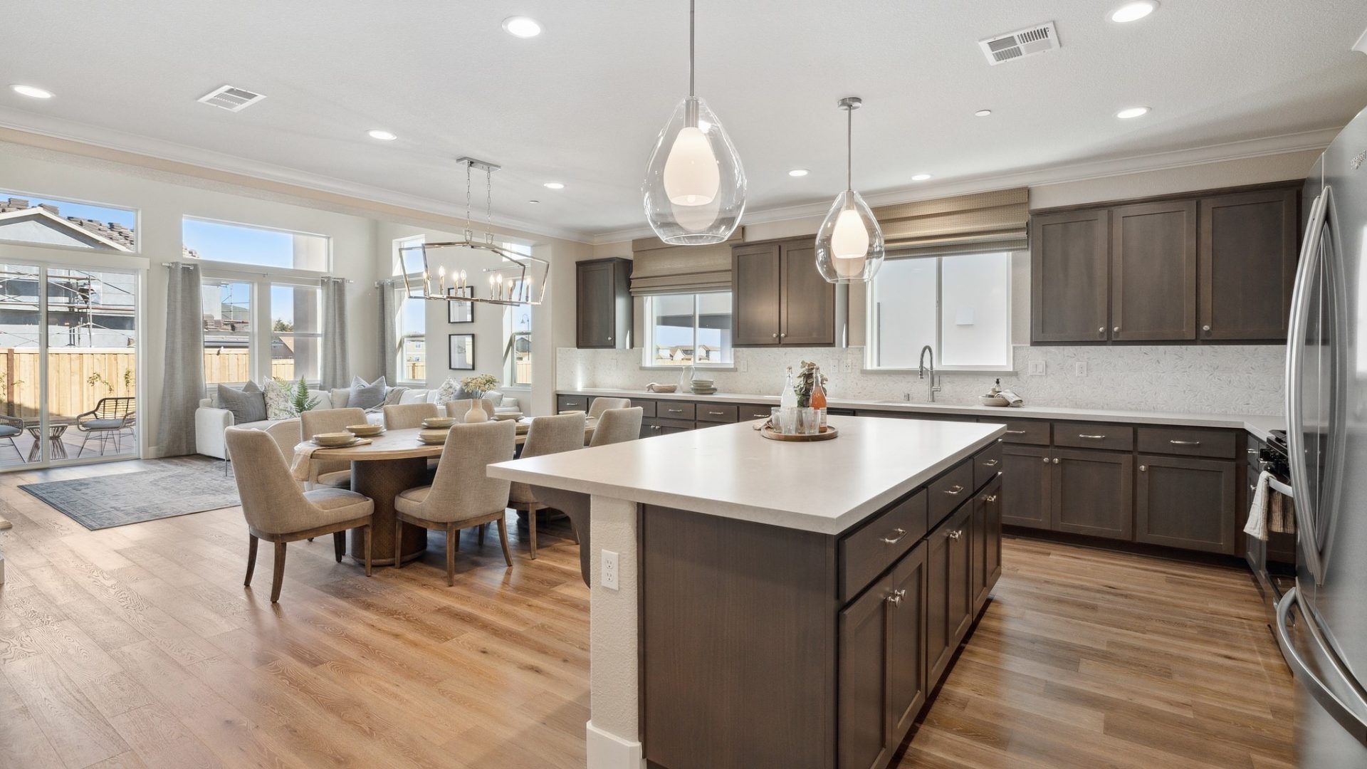 A large gourmet kitchen with a ton of cabinetry and countertop space with sterling silver appliances, dark brown stained cabinets, light colored countertops and full magma marble backsplash from the countertop to the bottom of the cabinets.