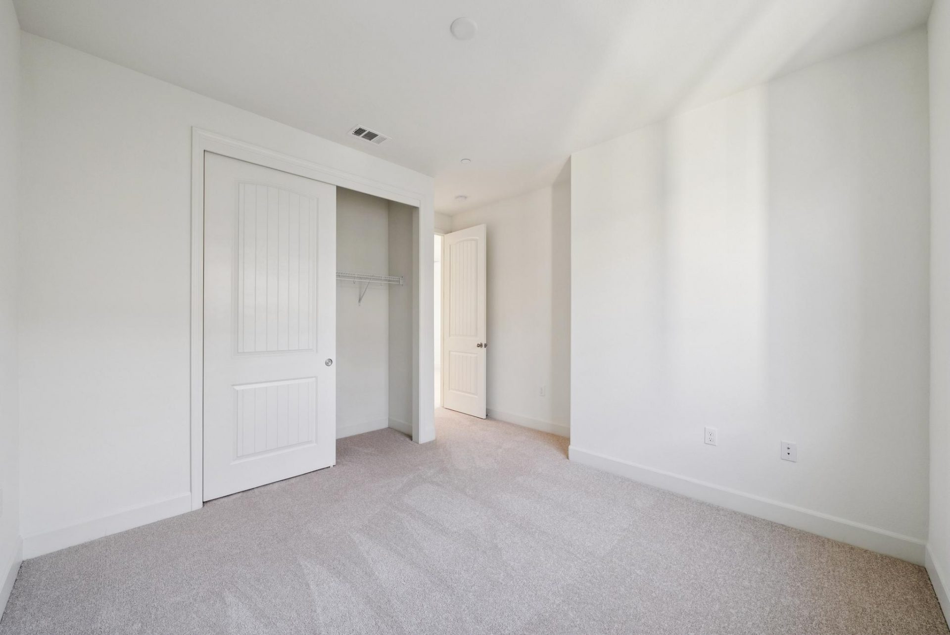 A bedroom with light colored carpet and a sliding door closet with light color walls.