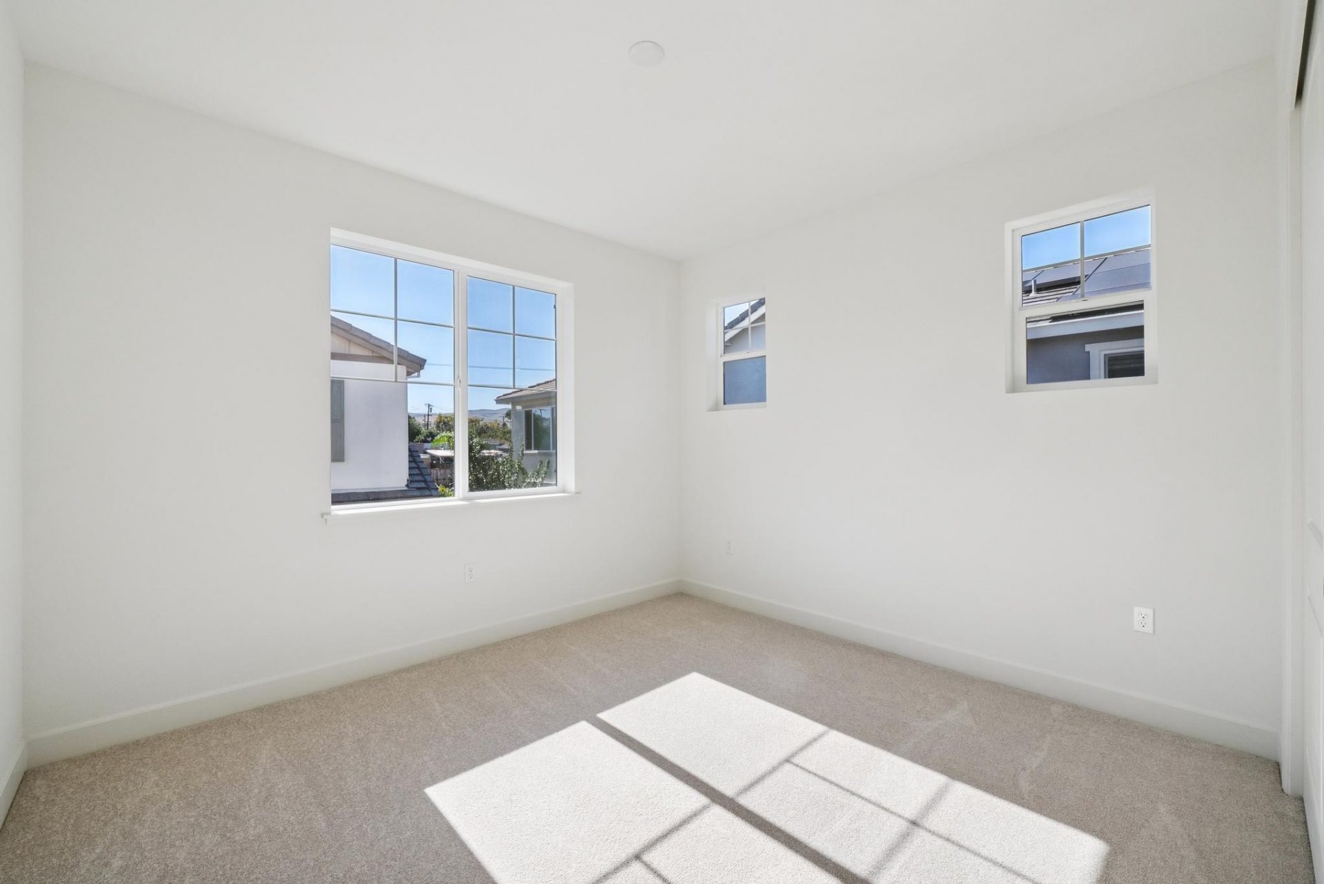 A bedroom with medium brown carpet and light colored walls, and three windows.