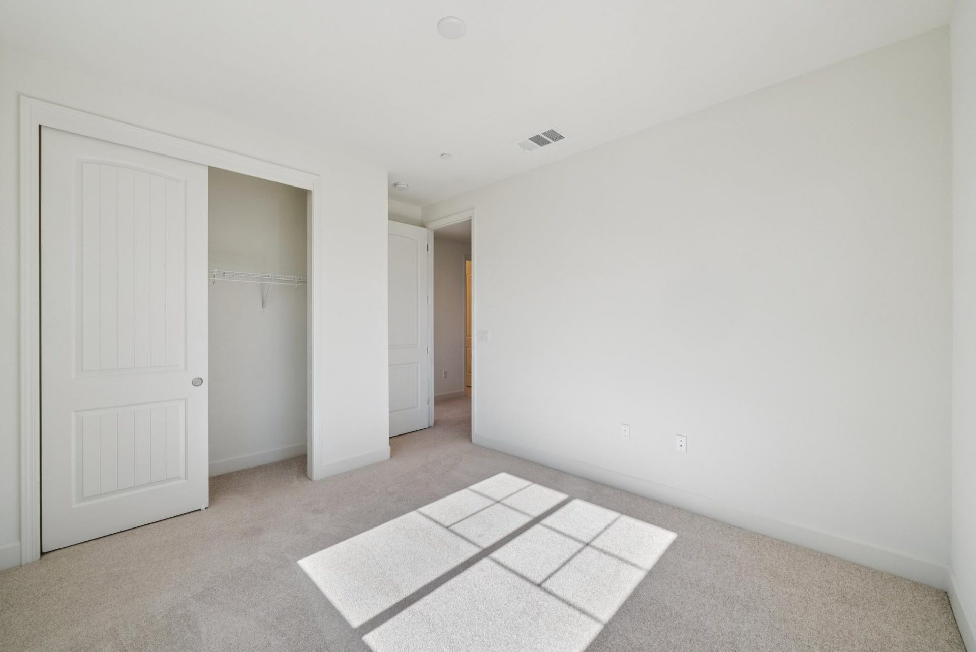 A bedroom with medium brown carpet and light colored walls, a sliding door closet and an open doorway.