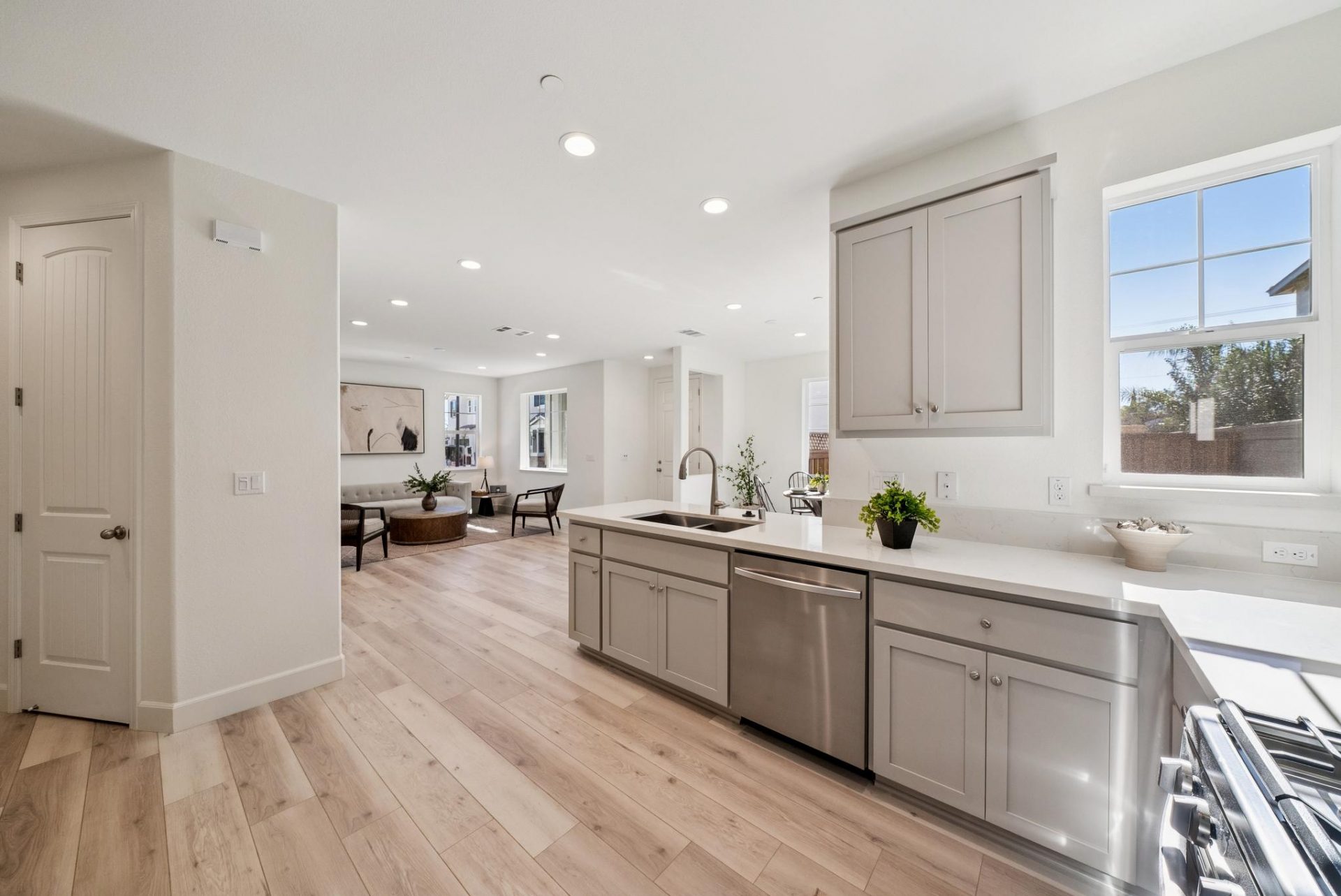 view from a kitchen looking out to family room, with light brown wood tone flooring, light brown cabinets, and light colored walls, with small pieces of décor.