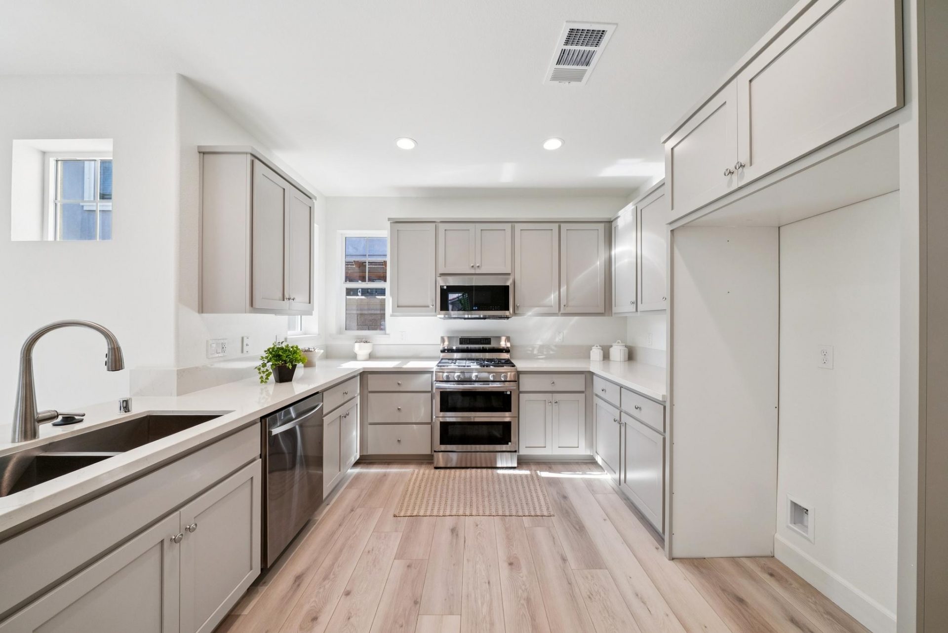 A kitchen with cabinetry on all sides of the room, a light gray paint color with stainless steel appliances and light colored countertops.