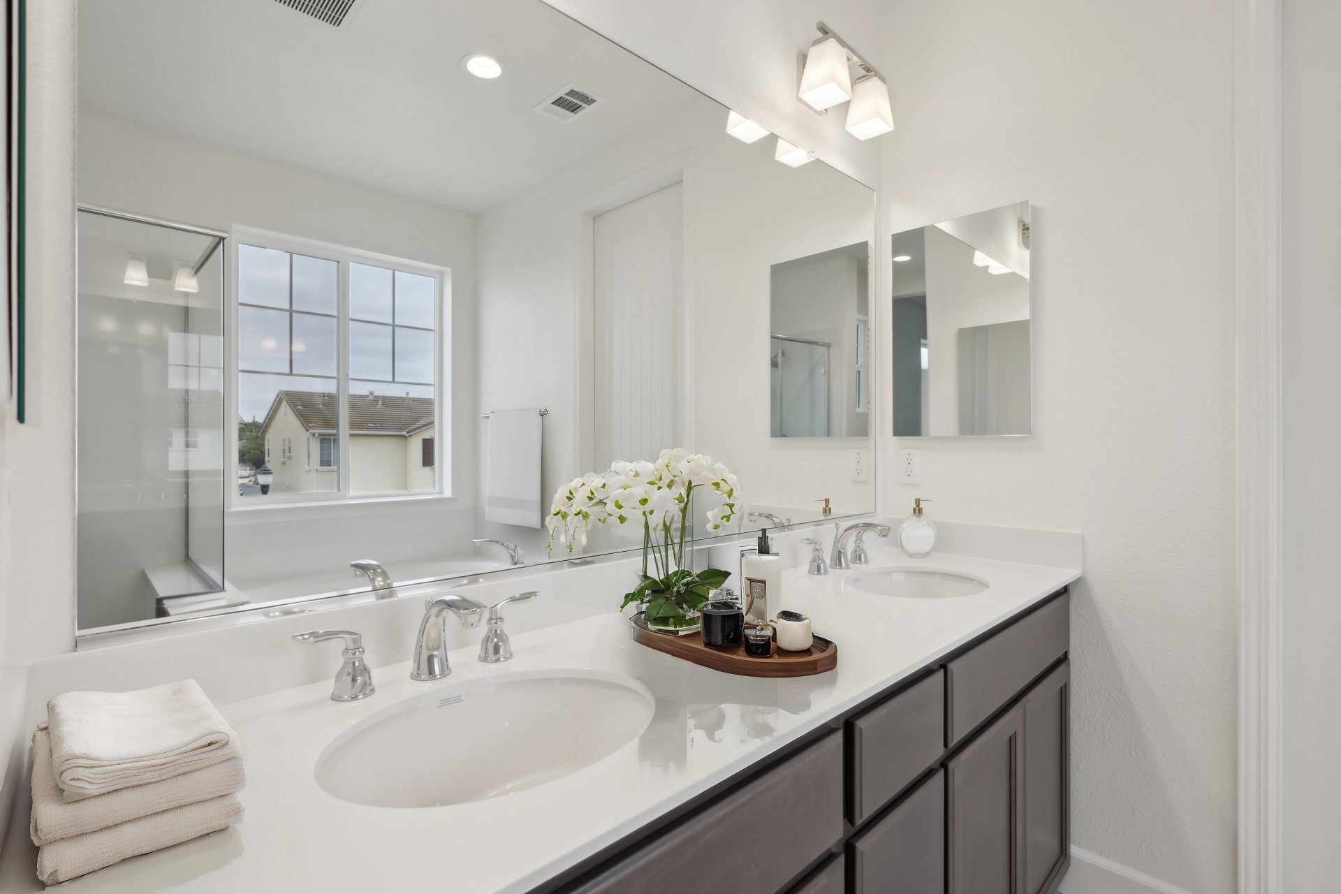 A virtually staged bathroom with dark brown cabinets and light countertops, double sink vanity with chrome fixtures and miscellaneous staged items on the countertop.