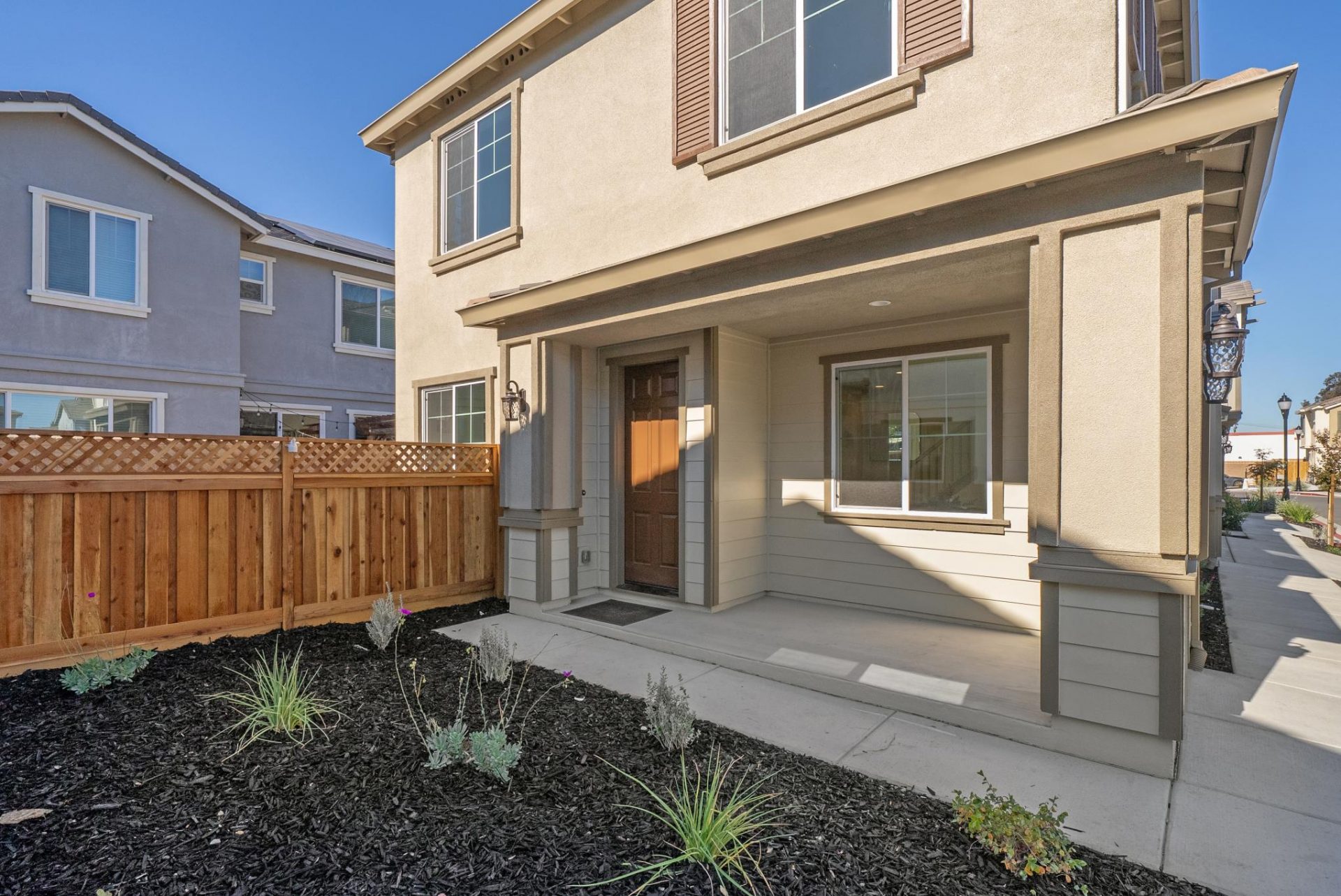 An exterior entry way to a modern home with light, medium and dark brown three color scheme, with mulch and plant landscaping.