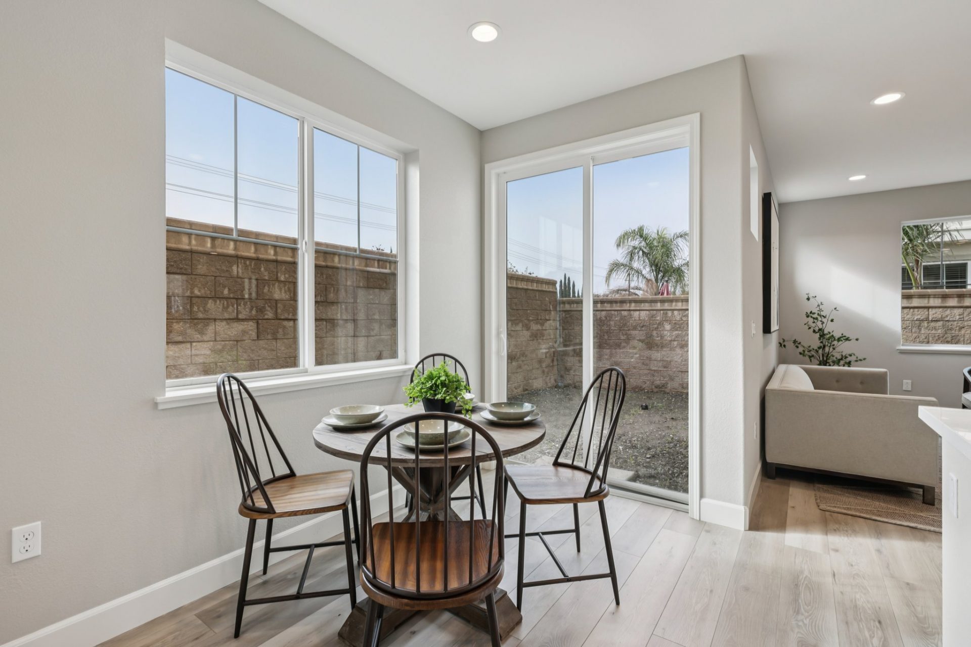 A dining nook staged with a round table with 4 wooden chairs, a large window and a sliding glass door provide an abundance of light to the area.