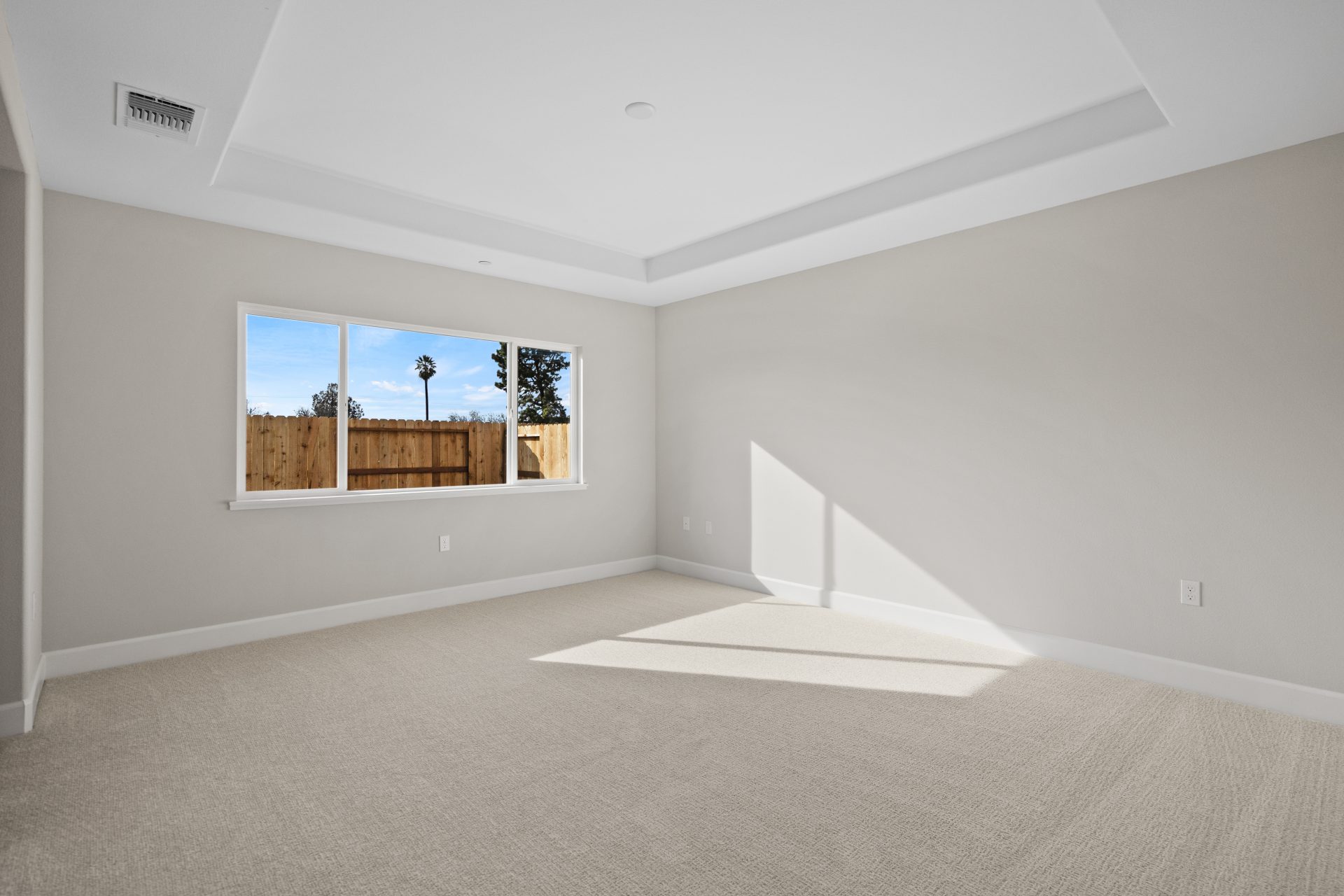 A large bedroom with light color carpet, medium color walls, a recessed ceiling and a large window.