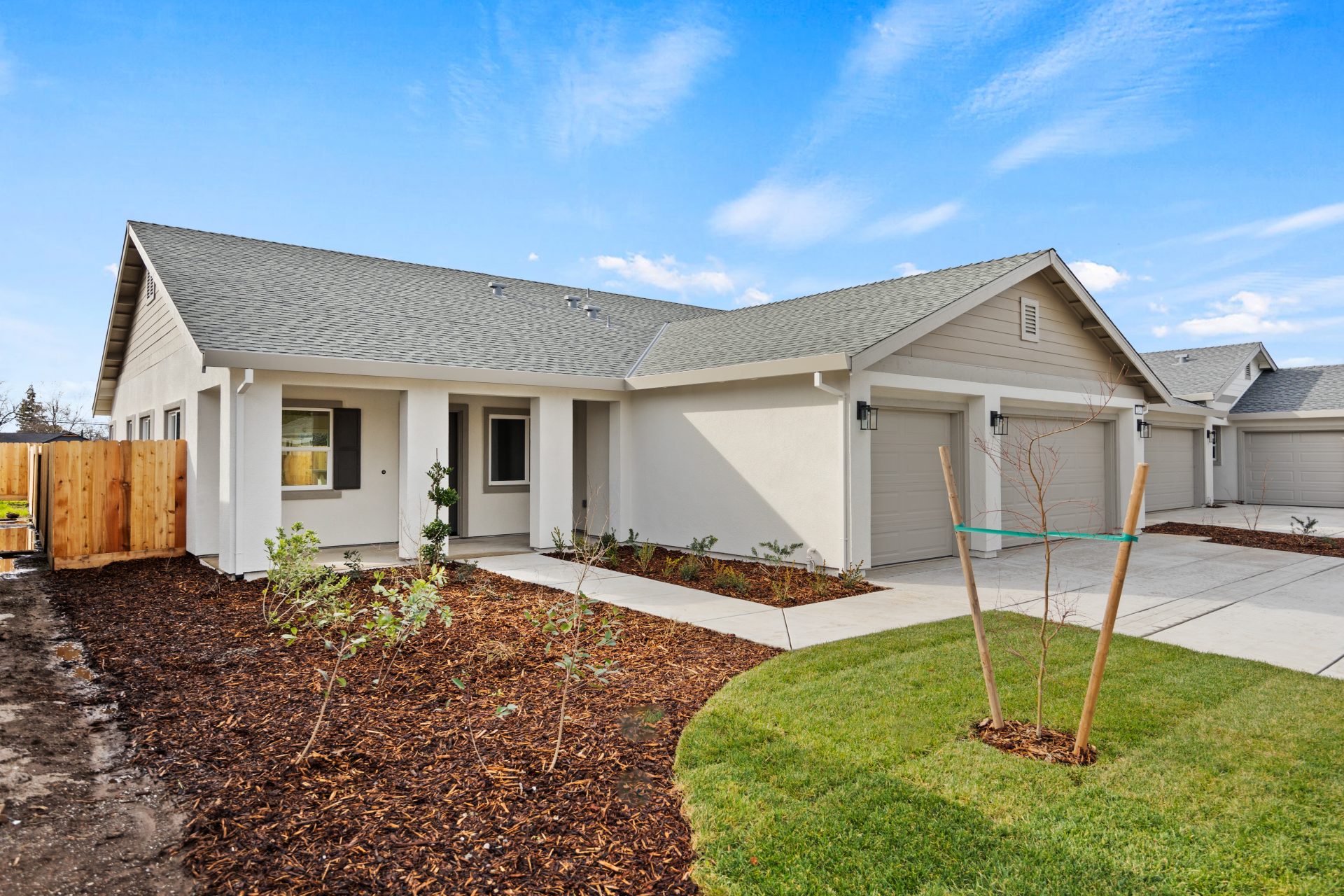 A side angle of the exterior of a single family home, single story with 3 car garage light body color with medium tan and khaki color accents. Front yard landscaping includes grass, mulch and shrubs.