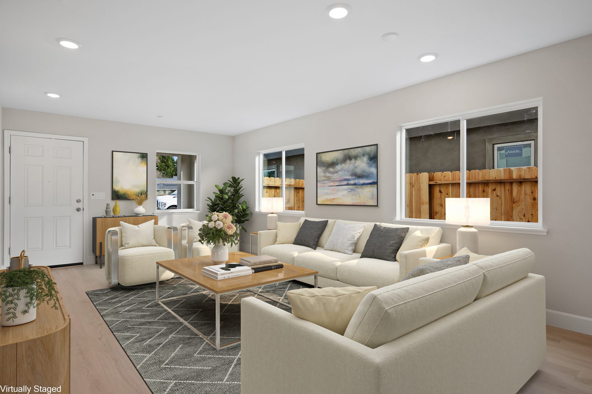 A virtually staged living room with white couches a charcoal area rug and charcoal throw pillows, a rectangular coffee table, various décor items and wall art.