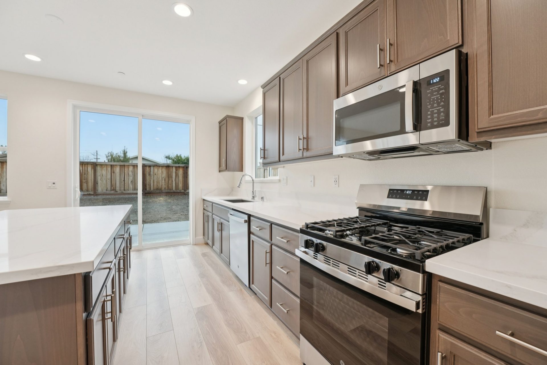 Kitchen with a gas stove, stainless steel appliances, brown stained upper, lower and island cabinetry with white color countertops.