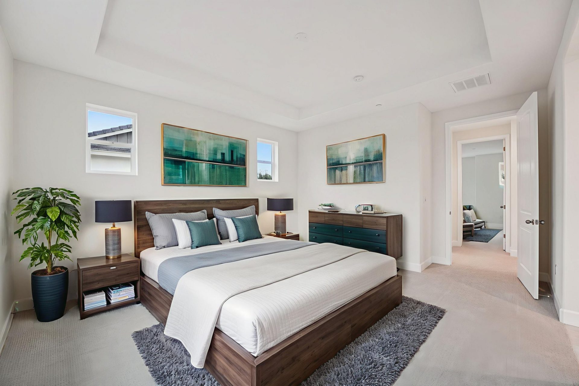 A bedroom virtually staged with a bedroom set including headboard and footrails, dresser and nightstands with lamps. There are two pieces of wall art and a potted plant in the corner.