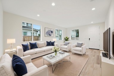 A family room virtually staged with a seating area with white couches and chairs with blue accent throw pillows, a coffee table, side tables and various items of décor.