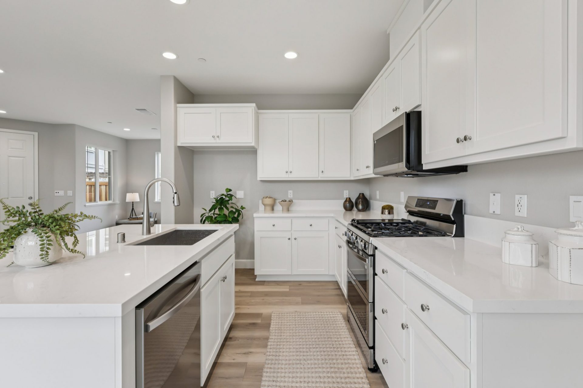 A view down a kitchen with an island on the left and upper and lower cabinets on right, White cabinets, white countertops and stainless steel appliances.