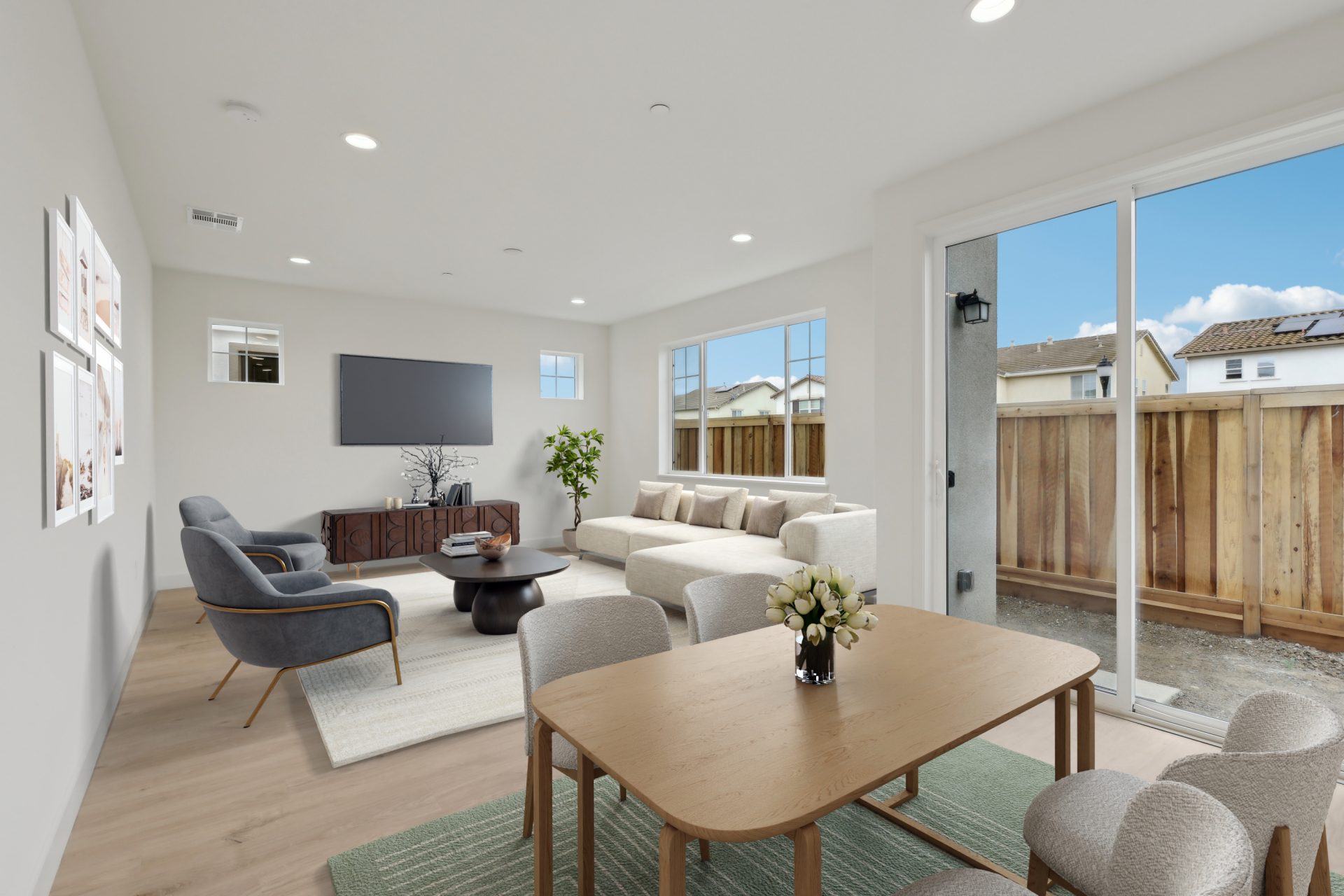 A virtually staged open concept area with a dining table and chairs with hardwood flooring, and a  family room with couches, chairs, area rug,  a tv stand and a wall mounted tv.