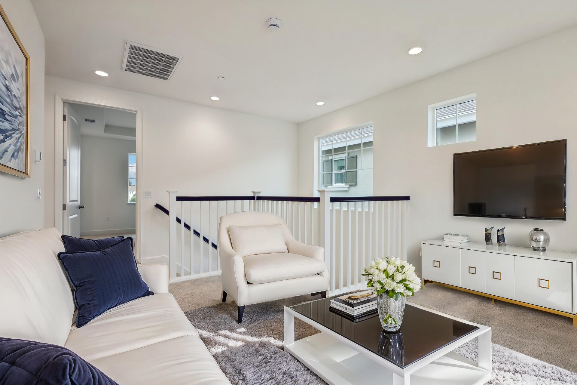 A loft area virtually staged with a white couch and chair, coffee table, tv and stand with small décor items.
