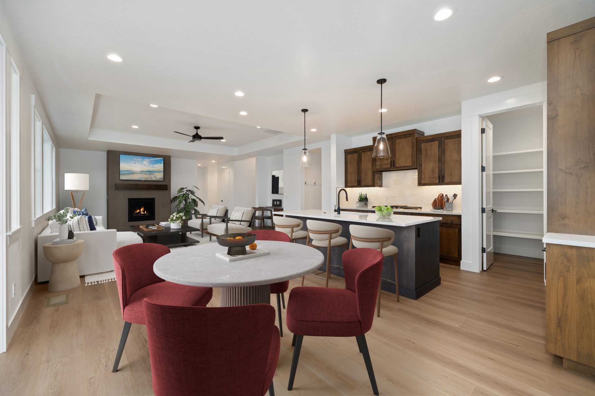 A virtually staged dining area featured in an open concept floorplan with a round table with four chairs, kitchen to the right and in the far scene a furnished family room.