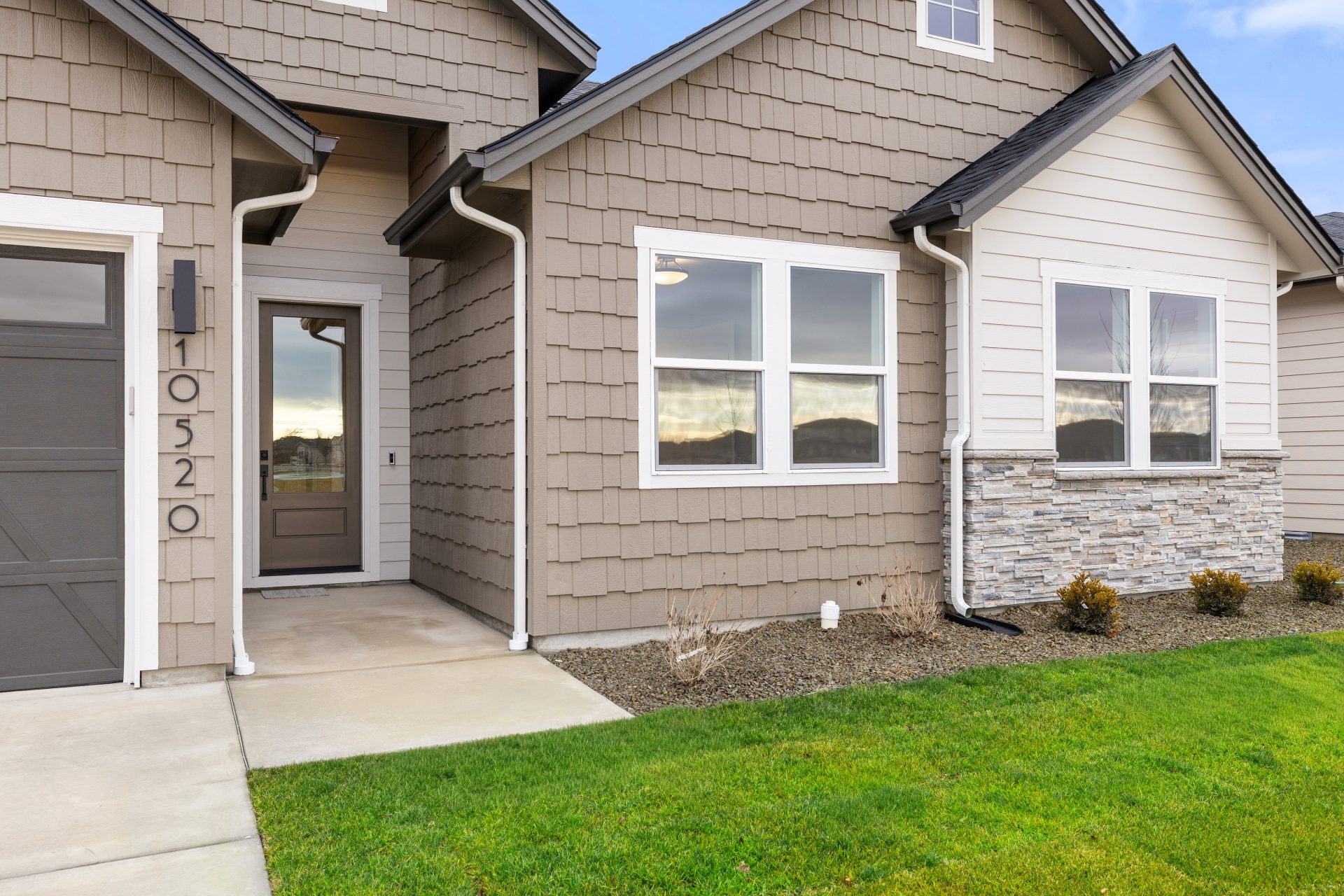 Exterior entry to a home with medium brown wood shingles, light color horizontal siding, stone detail at the bottom of the home and an entry door with a glass inset.