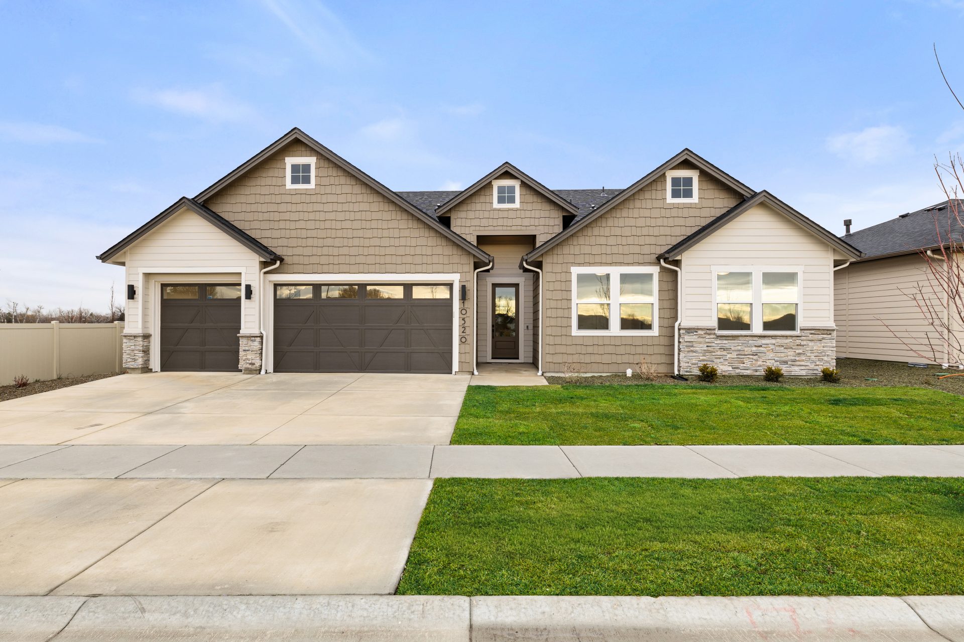 Exterior image of a single story home with wood shingles and horizontal siding, with a three car garage and a 3 color paint scheme of light, medium and dark brown, with stone detail at the bottom portion of home.