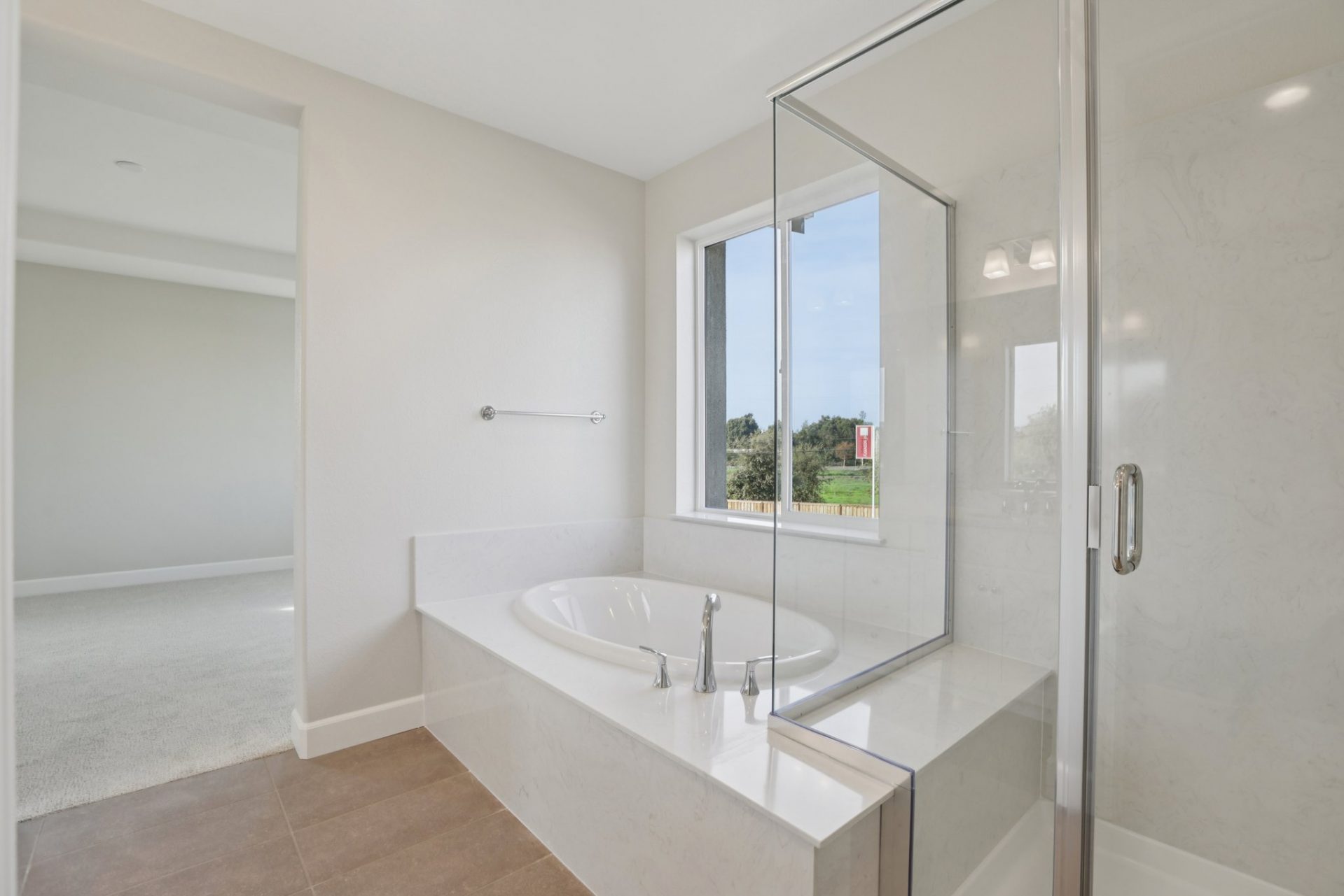 A bathroom with tan tile flooring, a white soak in tub and a shower with a glass enclosure and chrome fixtures.