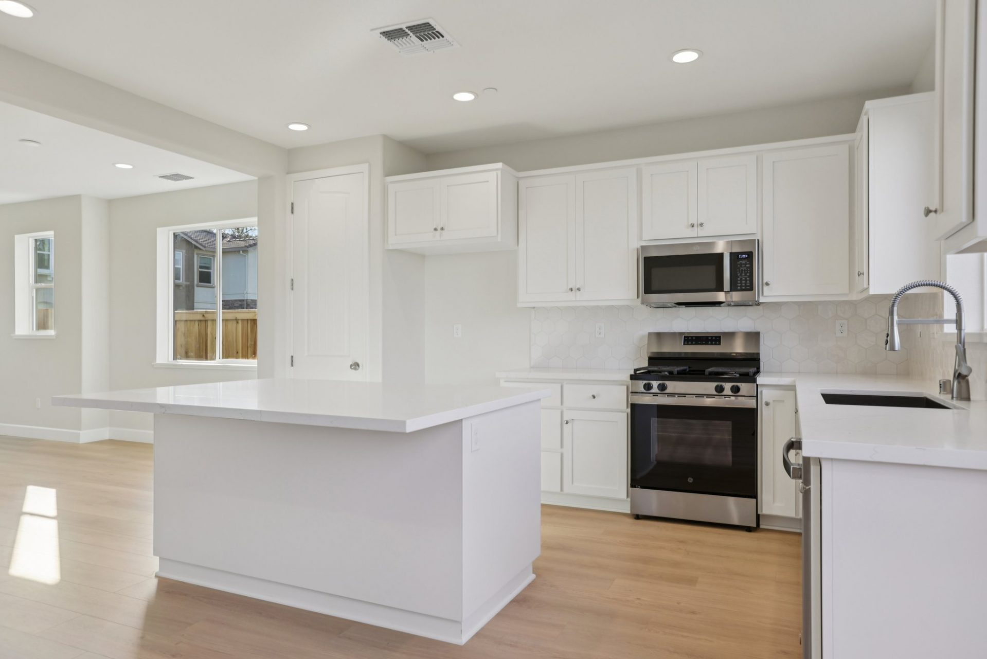 A kitchen with white upper and lower cabinets white countertops and light colored back splash from the counters to the upper cabinets, complete with a stainless steel gas stove and microwave hood.
