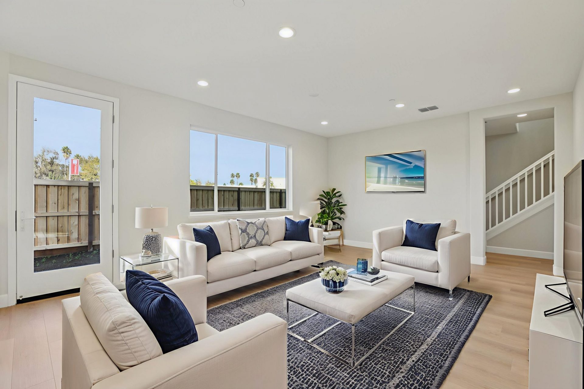 A virtually staged room with a seating area complete with a couch and two chairs, a rectangular coffee table, two  and an area rug with wall décor and a potted plant in the corner.