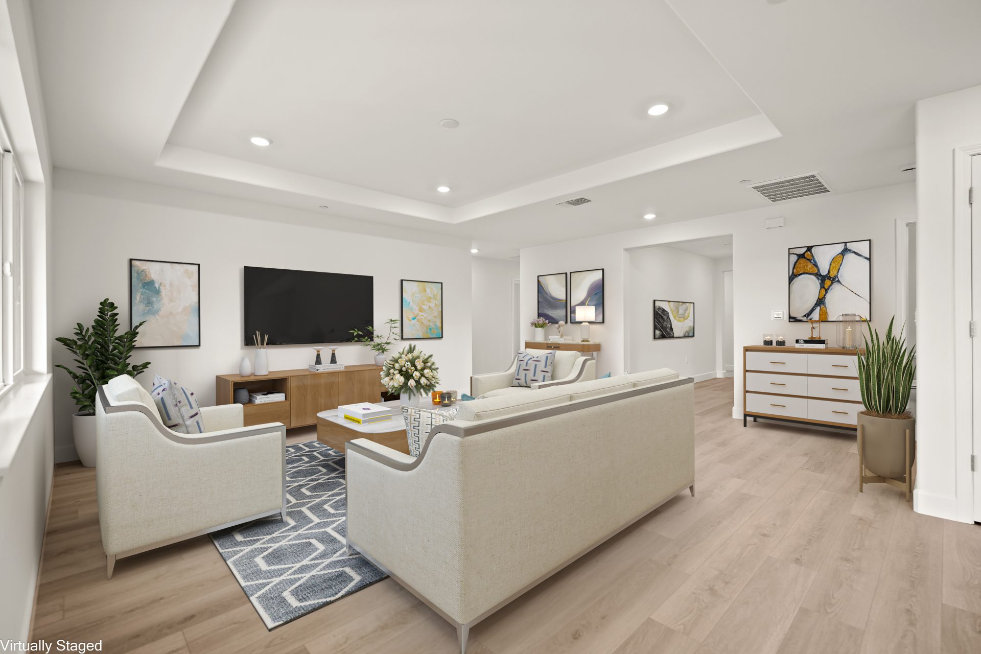 A virtually staged living area furnished with white couches and chairs, an area rug, credenza, tv stand and potted plants. A hanging tv and other wall art decorate the walls.