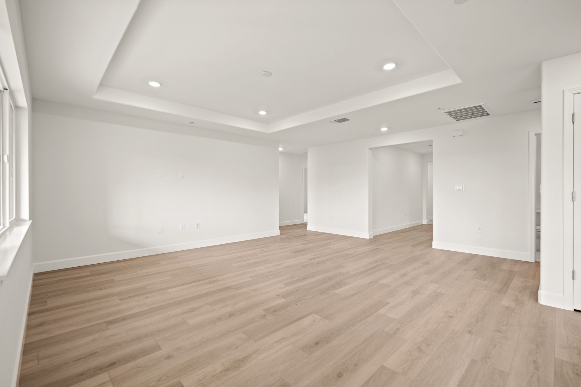 An unfurnished room with light wood flooring, light colored walls, and an inset ceiling with can lighting.