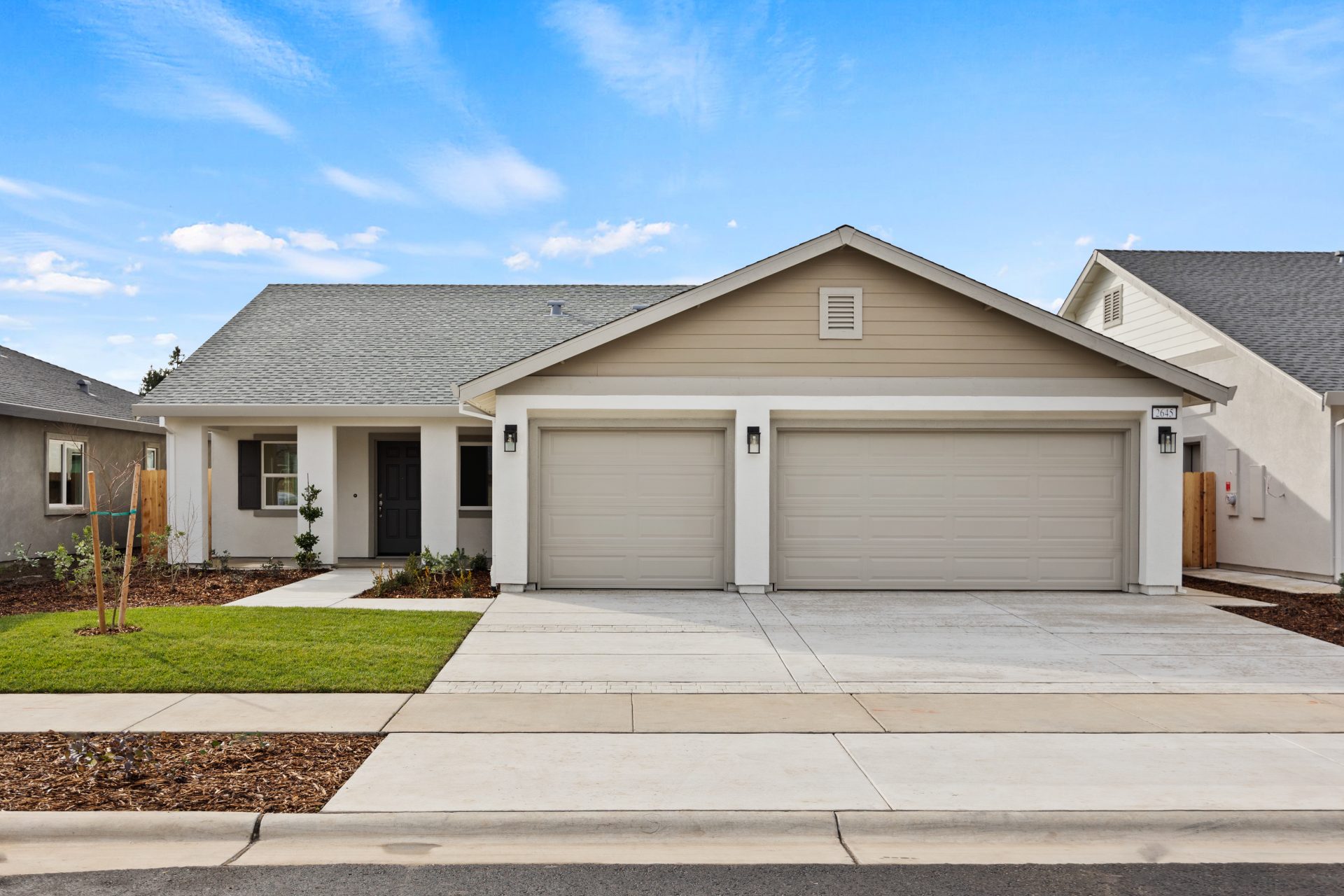 The exterior of a single family home, single story with 3 car garage light body color with medium tan and khaki color accents. Front yard landscaping includes grass, mulch and shrubs.
