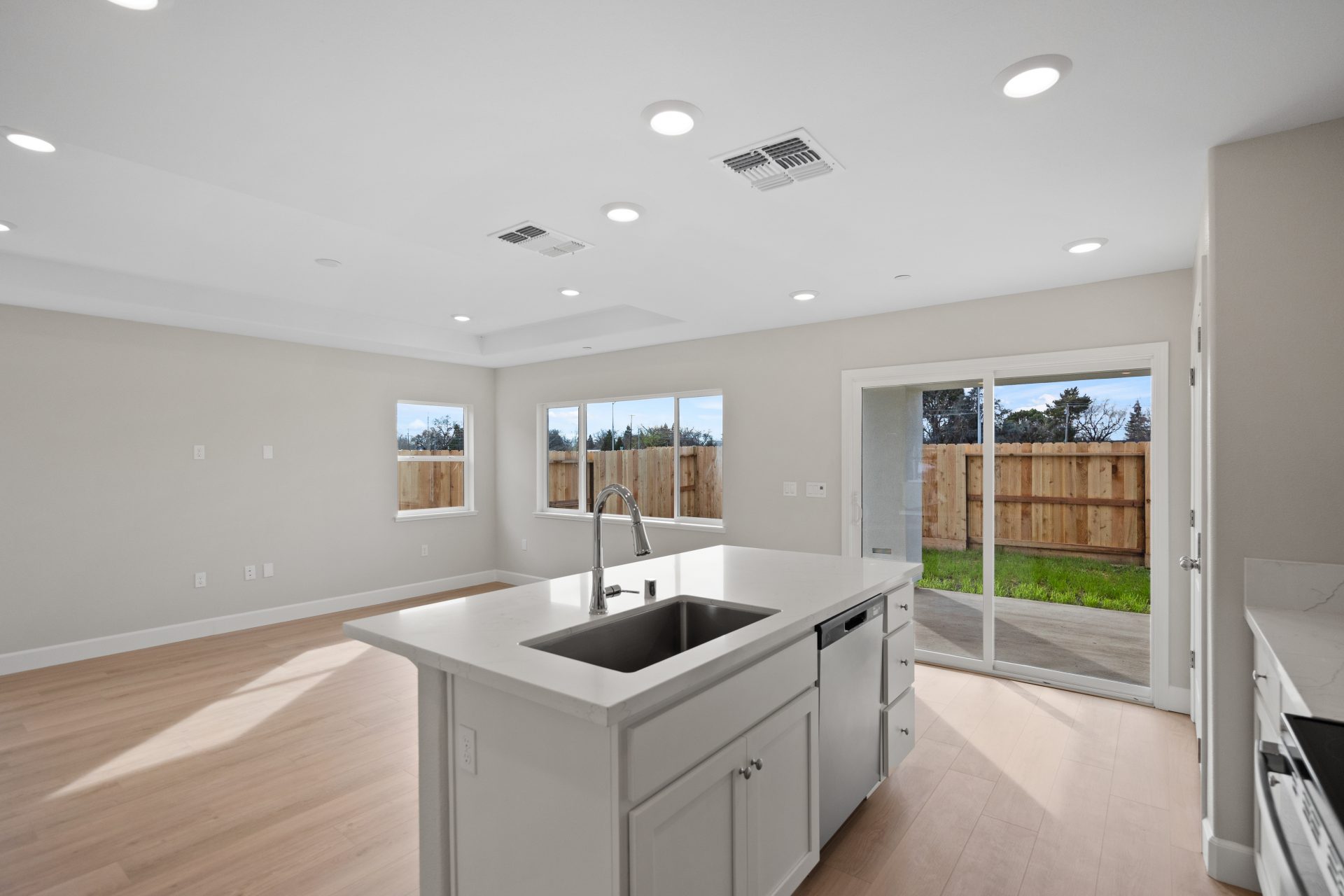 Angle from the kitchen looking outward over the kitchen island with a view of the dining/ living area and a view of the backyard through a window and sliding glass door.