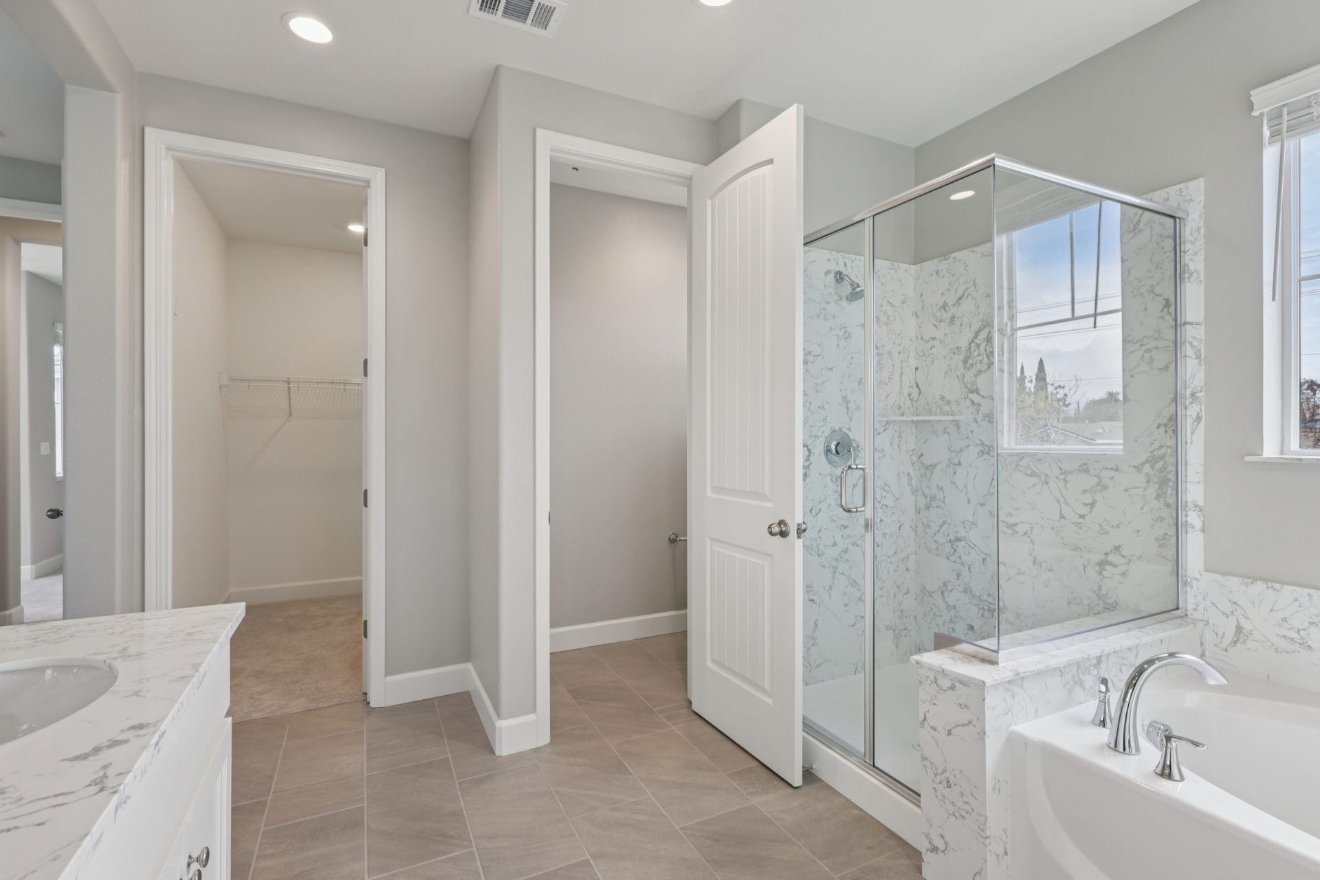 A bathroom with a shower with a glass enclosure, a soak in tub, a closet is seen in the distance.