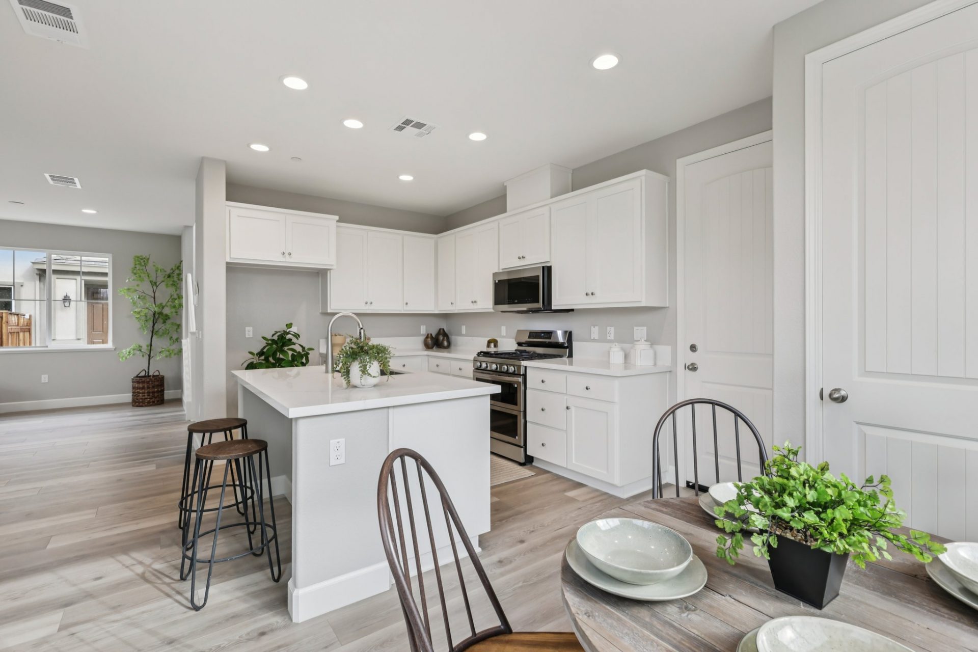 A dining area with a round table and chairs facing the kitchen, complete with white countertops and white cabinets, stainless steel appliances and a kitchen island.
