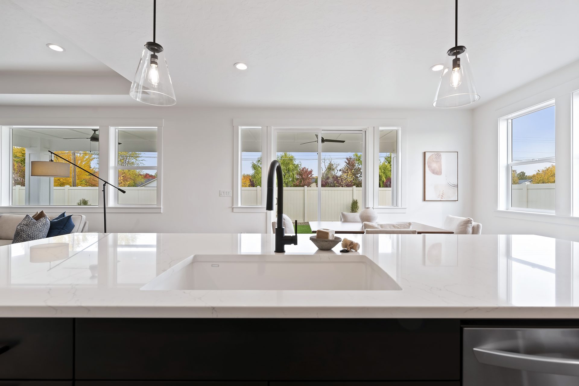 View of the dining area from behind the kitchen island looking over the sink with black faucet, there are two glass pendant lights hanging above the kitchen island.