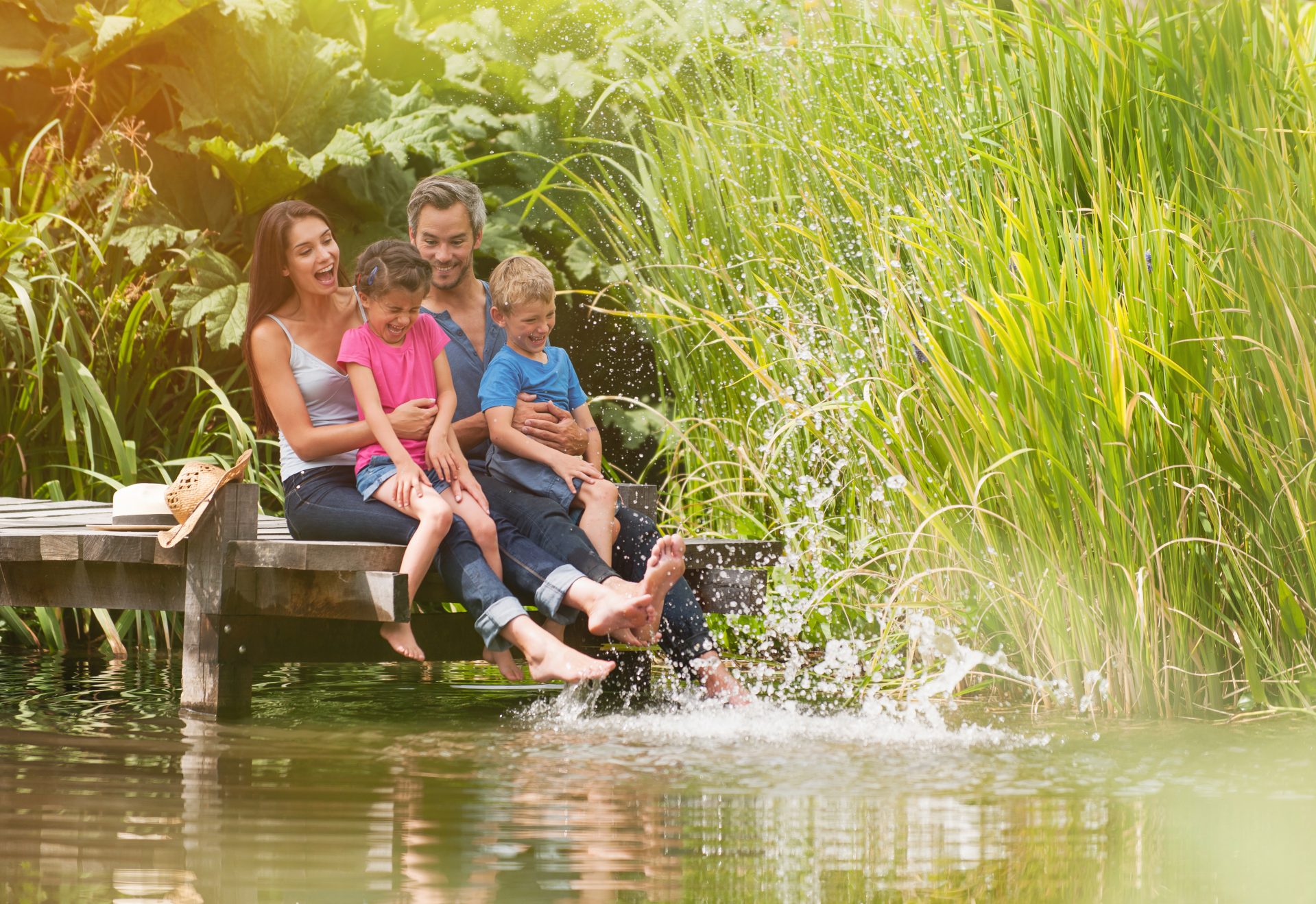 Family of four sitting on a dock at a lake splashing their feet in the water below