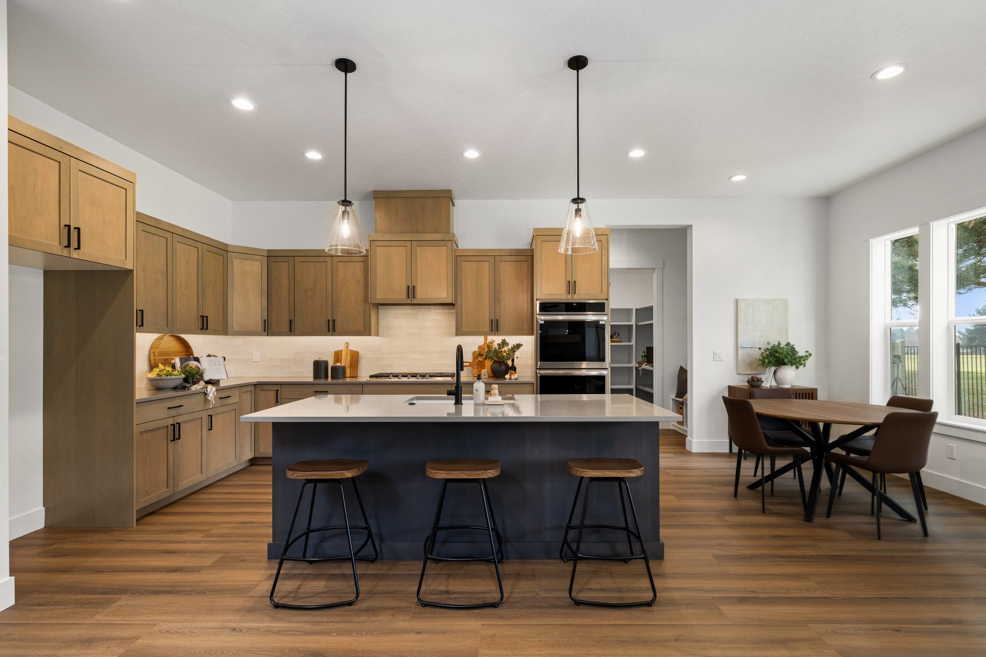 Modern kitchen and dining room with wooden cabinetry, double-oven, pendant light fixtures, and center island