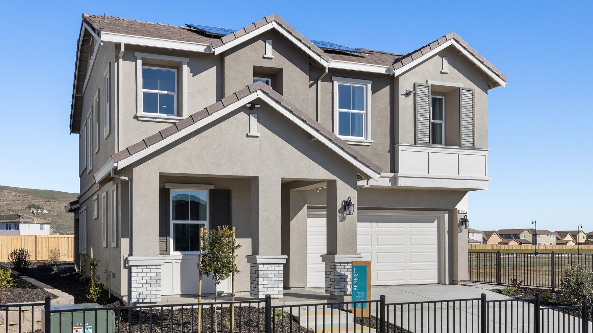 Exterior of a home with multiple roof peaks, with a 3 color paint scheme, with a mix of light and dark grays and an off-white color garage door. There are 3 pillars at the entry way with brick detail towards the bottom with mulch and plant landscaping.