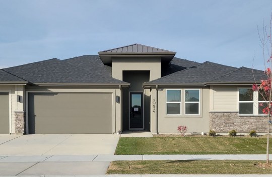 Exterior of a home with a medium brown and dark brown color scheme, dark roof and stone detail around the bottom half of the house. Grass, rock and small plant landscaping.