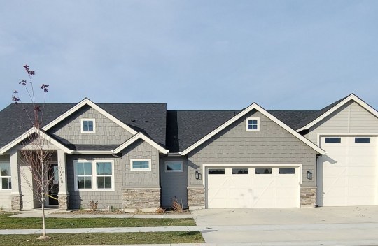 Exterior of a home with wood shingles and stone accents on the lower half of the home. A two car + RV garage with a medium gray, light gray and off white color scheme.