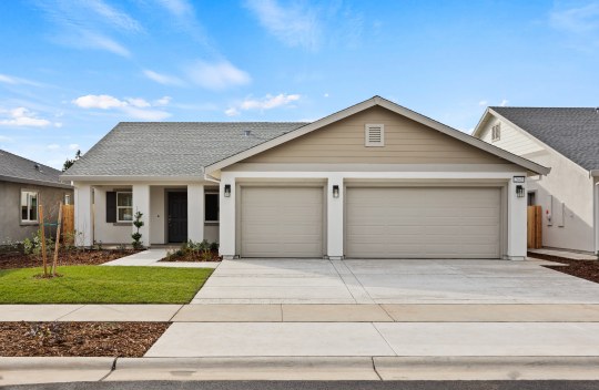 The exterior of a single family home, single story with 3 car garage light body color with medium tan and khaki color accents. Front yard landscaping includes grass, mulch and shrubs.