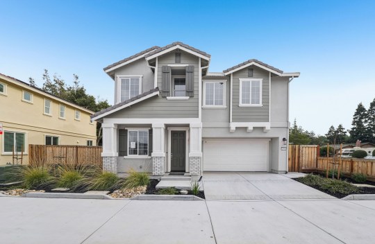 An exterior view of a two story home with a gray and white color scheme with stone detail near the front entry with dark mulch and small bushes for landscaping.