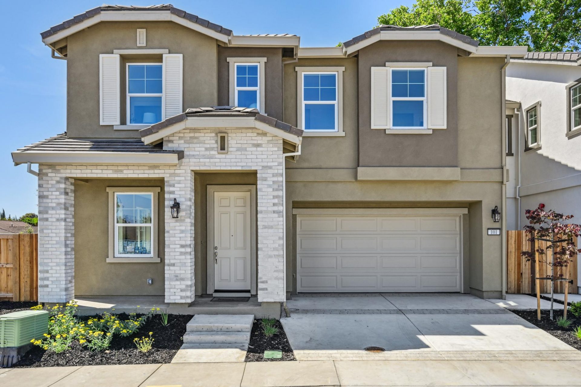 Exterior photo of  a modern two story home with stone detail at the entry, brown and tan color scheme, two car garage and mulch with shrub landscaping.
