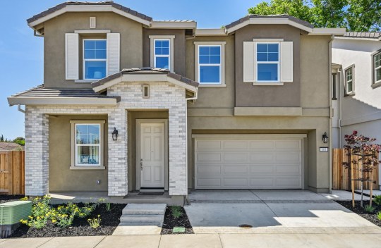 Exterior photo of  a modern two story home with stone detail at the entry, brown and tan color scheme, two car garage and mulch with shrub landscaping.