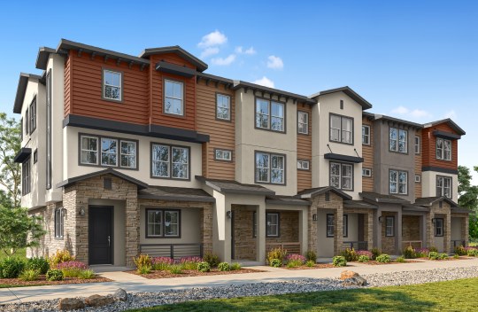 Modern row of three-story townhouses with mixed siding and stone accents, featuring large windows, small front porches, and landscaped greenery under a blue sky